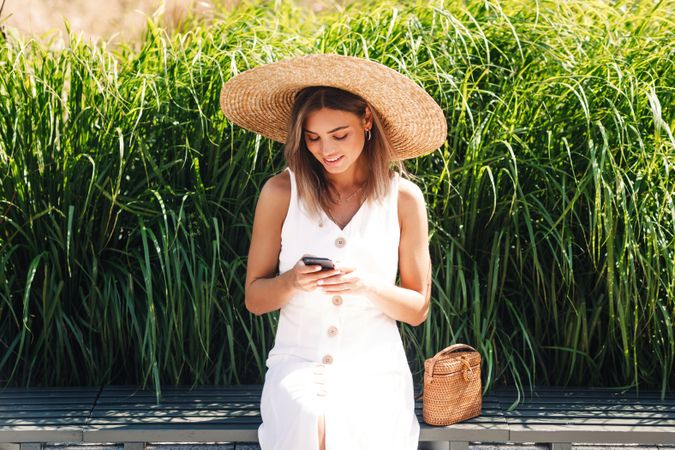 Woman sitting in front of long grass looking down at her cell phone