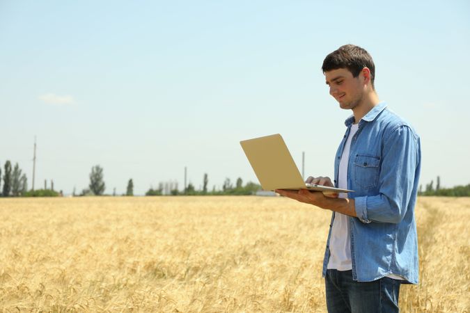 Young man with laptop in barley field. Agriculture business. Farming