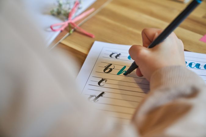 Crop unrecognizable artist drawing letters sitting at wooden table