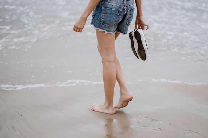 Young female walking barefoot on wet sand