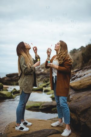 Happy female friends blowing bubbles on seashore