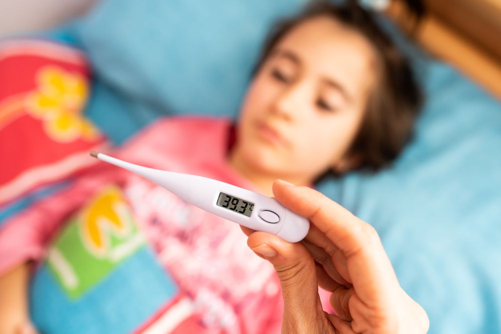 Girl in bed with adult taking her temperature