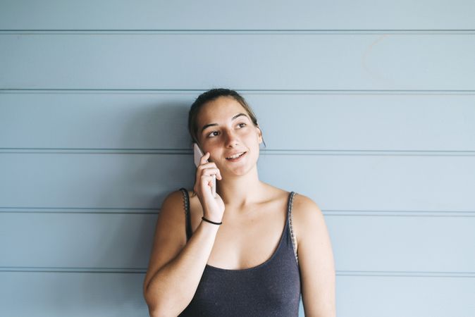 Teenage female in summer dress talking on cell phone while leaning against wood paneled wall