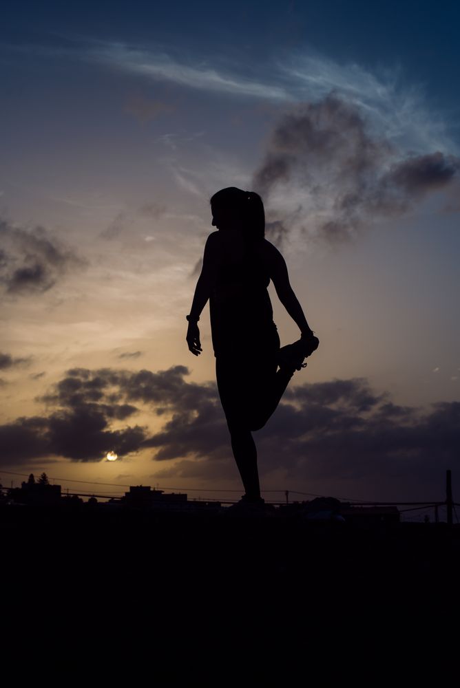 Stretching woman and sky with clouds at sunset