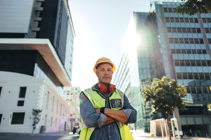 Confident construction contractor standing in front of high rise buildings with arms crossed