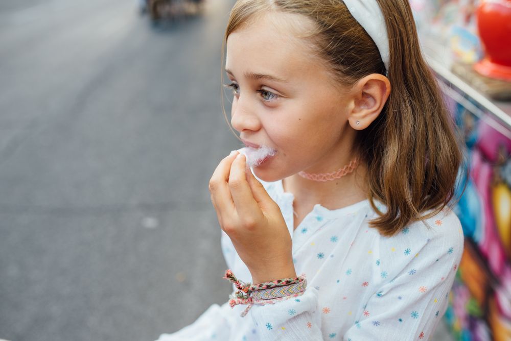 Cheerful girl eating cotton candy on street