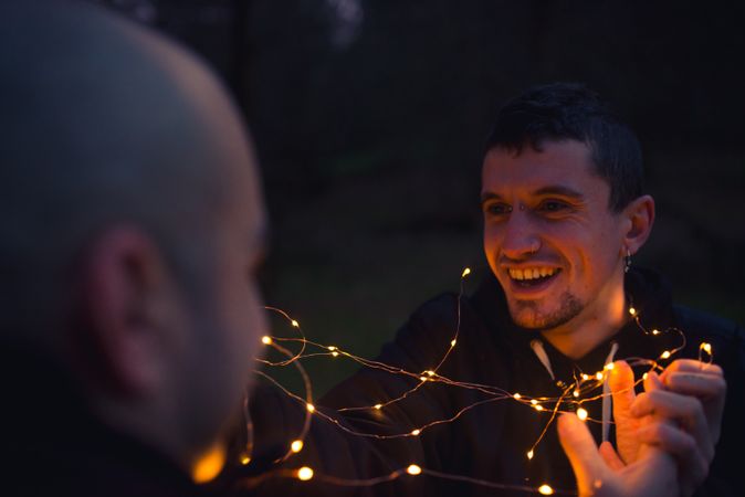 Men unwrapping fairy lights in forest at night