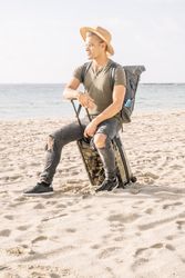 young latino man with a modern look and hat on miami beach with a travel suitcase