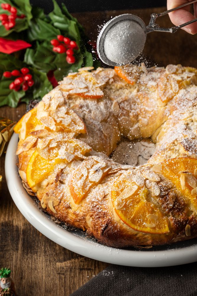 Person dusting powdered sugar over a cake with orange slices