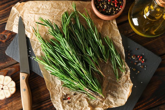 Composition with rosemary, oil, pepper, garlic and knife on wooden table, top view