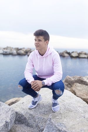 Young teenager male leaning down on breakwater rocks while looking away