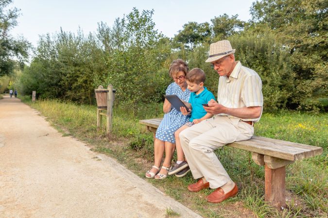 Grandchild and grandmother using a tablet outdoors with male child