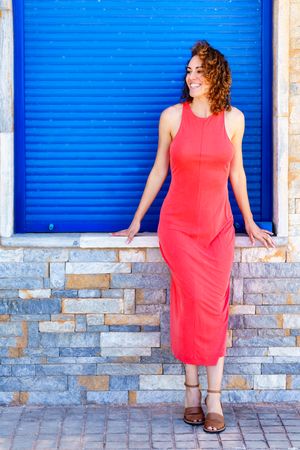 Carefree woman in summer dress leaning on brick wall in front of blue shutter
