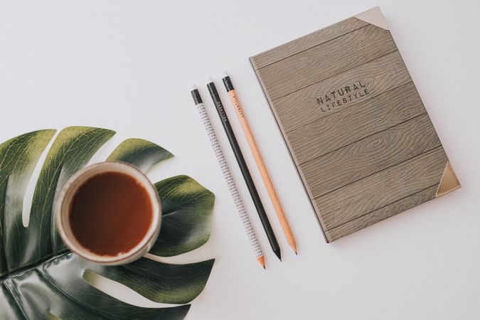 Writing accessories and drink in mug on palm leaf