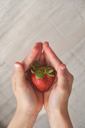 Faceless child holding red strawberry in cupped hands