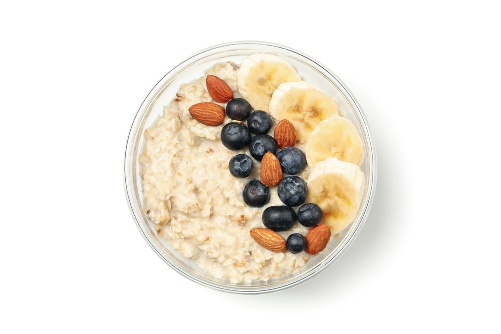 Bowl with oatmeal porridge and ingredients isolated on plain background