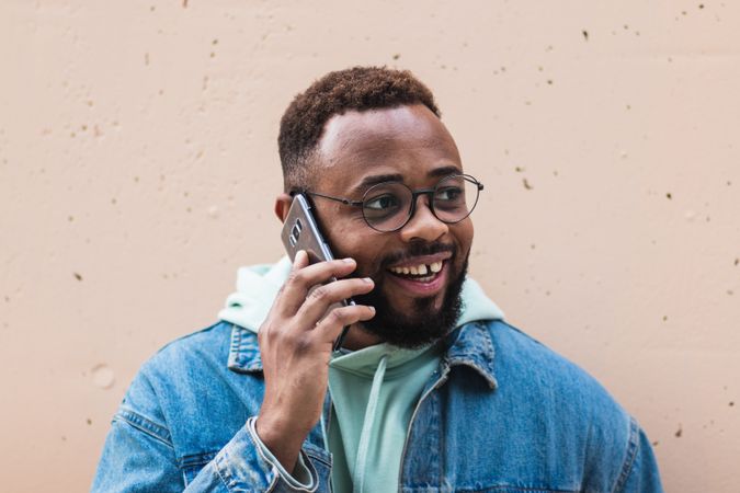 Cheerful Black man talking on phone near wall