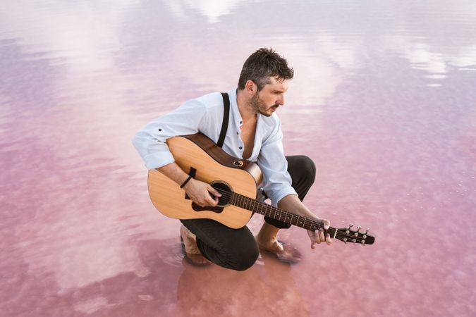 Musician with guitar on pink sandy water