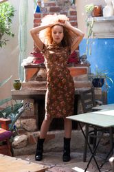 Young Black woman in brown dress standing in front of outdoor fireplace