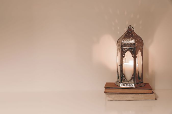 Silver burning Moroccan lantern, old books on wooden table with copy space. Ramadan Kareem muslim holiday still life. Neutral beige wall background. Elegant Iftar dinner. Festive celebration.