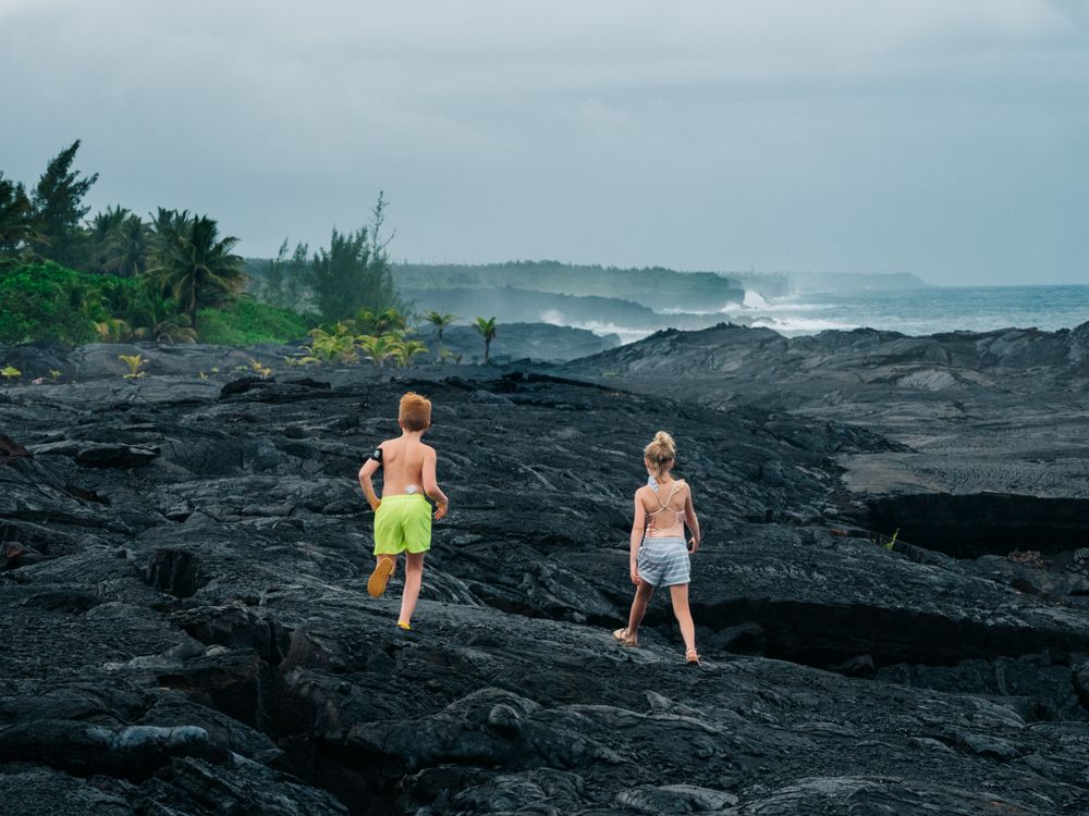 Girl and boy walking on dark rocks on seashore