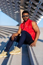 Black man wearing sunglasses and red vest sitting on staircase outside