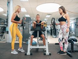 Young women helping man to lift barbell