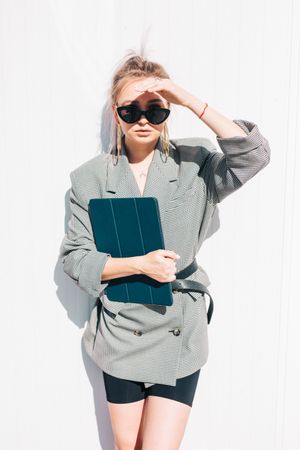 Stylish businesswoman with laptop leaning on wall