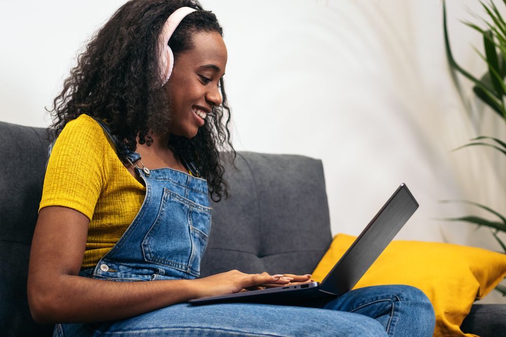 Young Black woman working with laptop and enjoying music at home