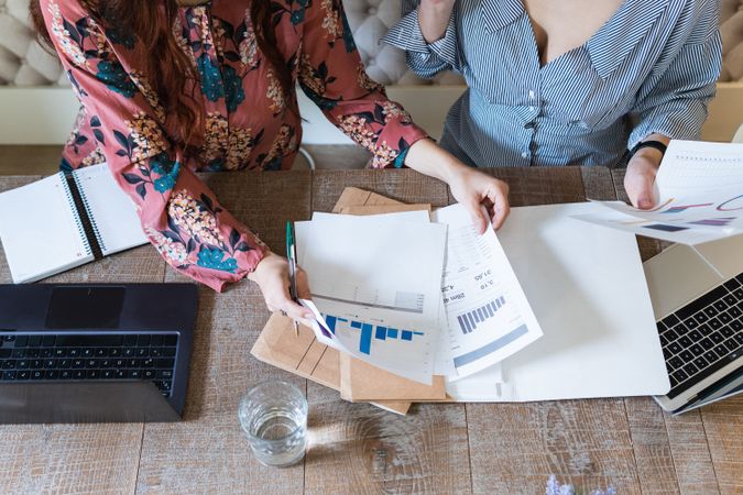 Crop focused female colleagues analyzing charts together in office