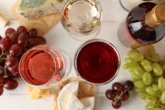 Grape, cheese, bottle and glasses with wine on light background, top view