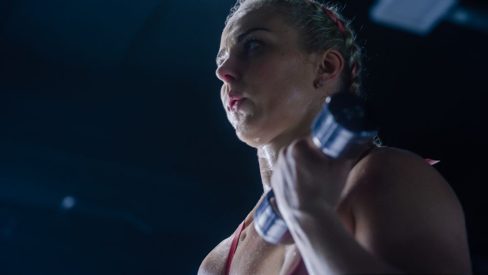 A Female Kickboxer Building her Arms' Muscles Using Dumbbell Exercises in an Empty Hardcore Gym.