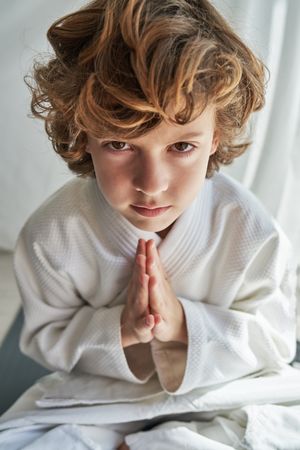 Serious boy in kimono practicing yoga in Lotus pose with namaste