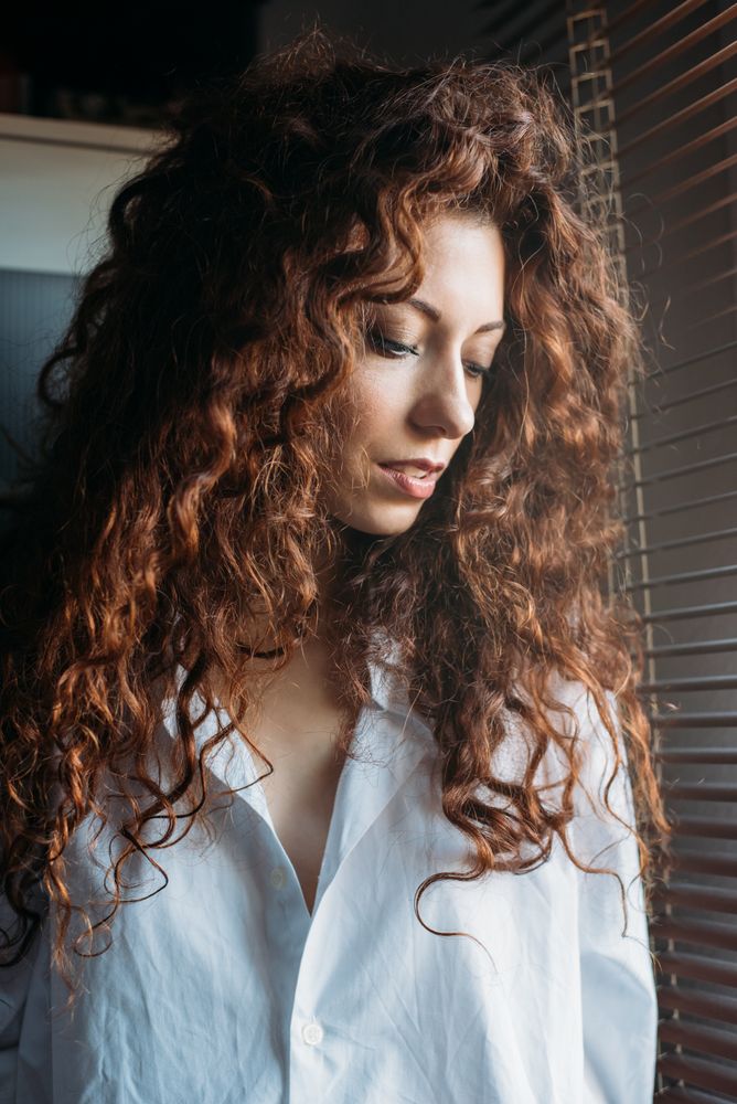 Beautiful thoughtful woman standing by a windows blind