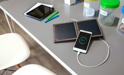 Mobile phone charging with portable solar panel and selective trash bins over desk in classroom