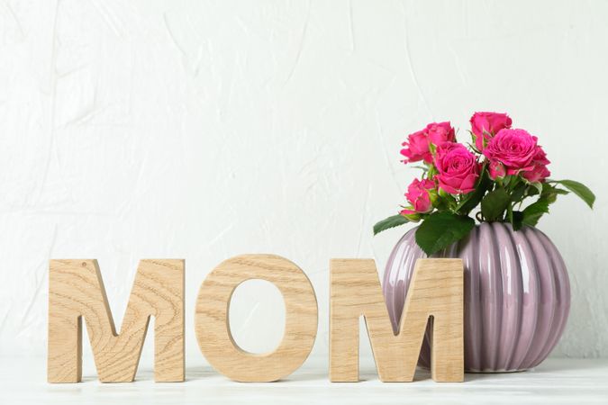 Inscription Mom and vase with pink roses on table, space for text