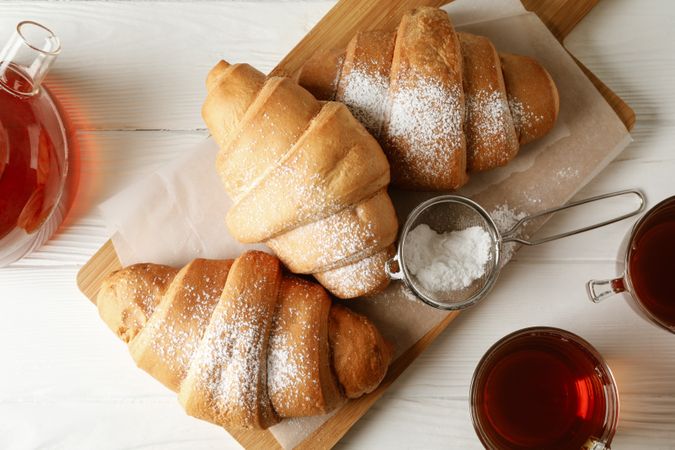 Looking down at tasty croissants and cups with tea on wooden cutting board