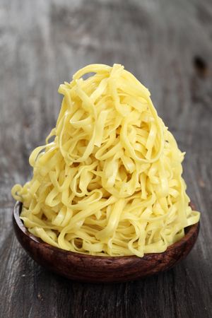 Close Up A Pile of Yellow Flat Noodle on Wooden Bowl