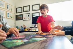 Cheerful little boy playing jigsaw puzzle with crop parents at home