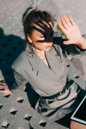 Woman sitting on asphalt with tablet and closing from sun