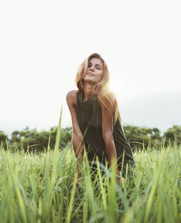 Portrait of attractive young lady sitting in the field of tall grass on a summer day