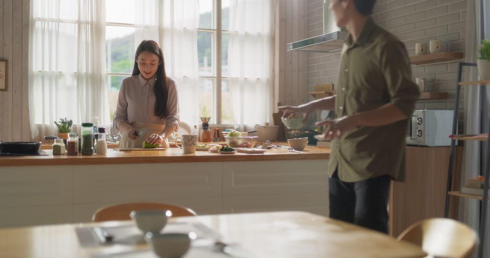 Female Cutting Vegetables with a Chef's Knife, Boyfriend Talking with Her, Making Jokes While Arranging the Table