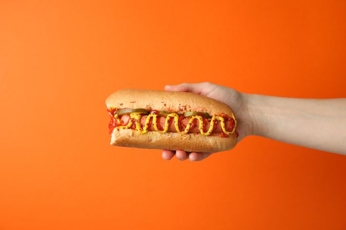 Hand holds tasty hot dog on orange background