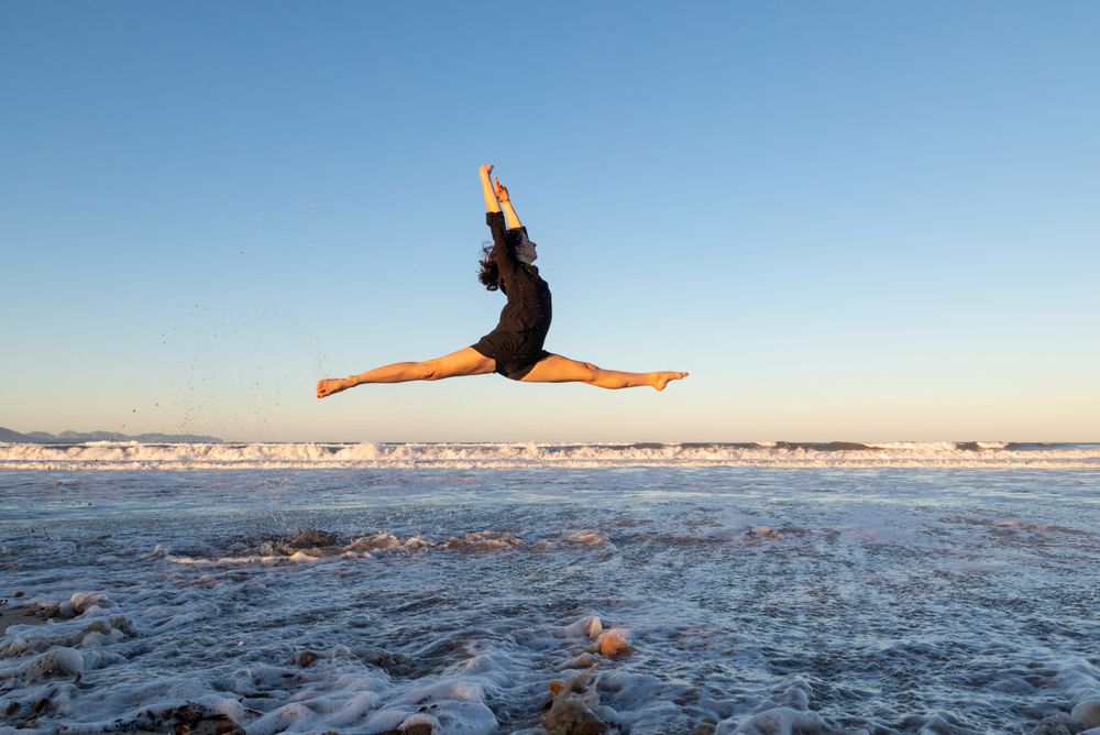 Woman jumping near water on shore
