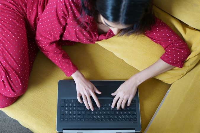 Woman relaxing at home using laptop on yellow sofa