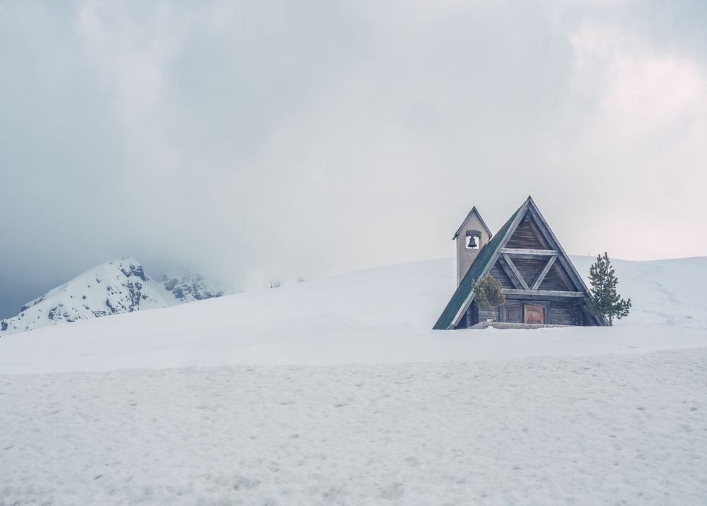 Wooden house with triangular roof located on snowy hill