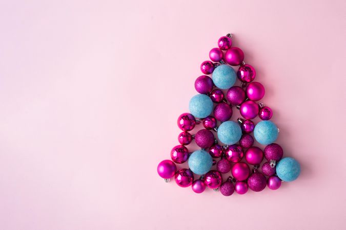 Arrangement of pink and blue festive baubles in shape of tree on pink background
