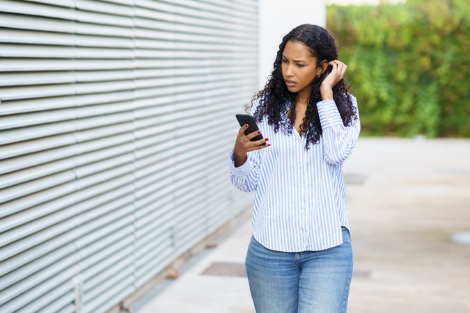 A young woman is fully engaged with her smartphone while standing in a vibrant urban setting