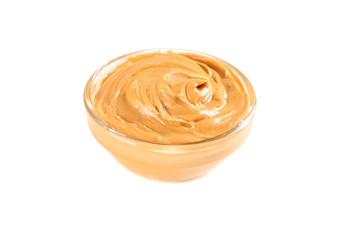 Creamy peanut butter in glass bowl isolated on light background. A traditional product of American cuisine