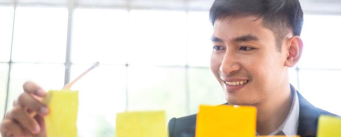 Smiling male using sticky notes on glass to brainstorm